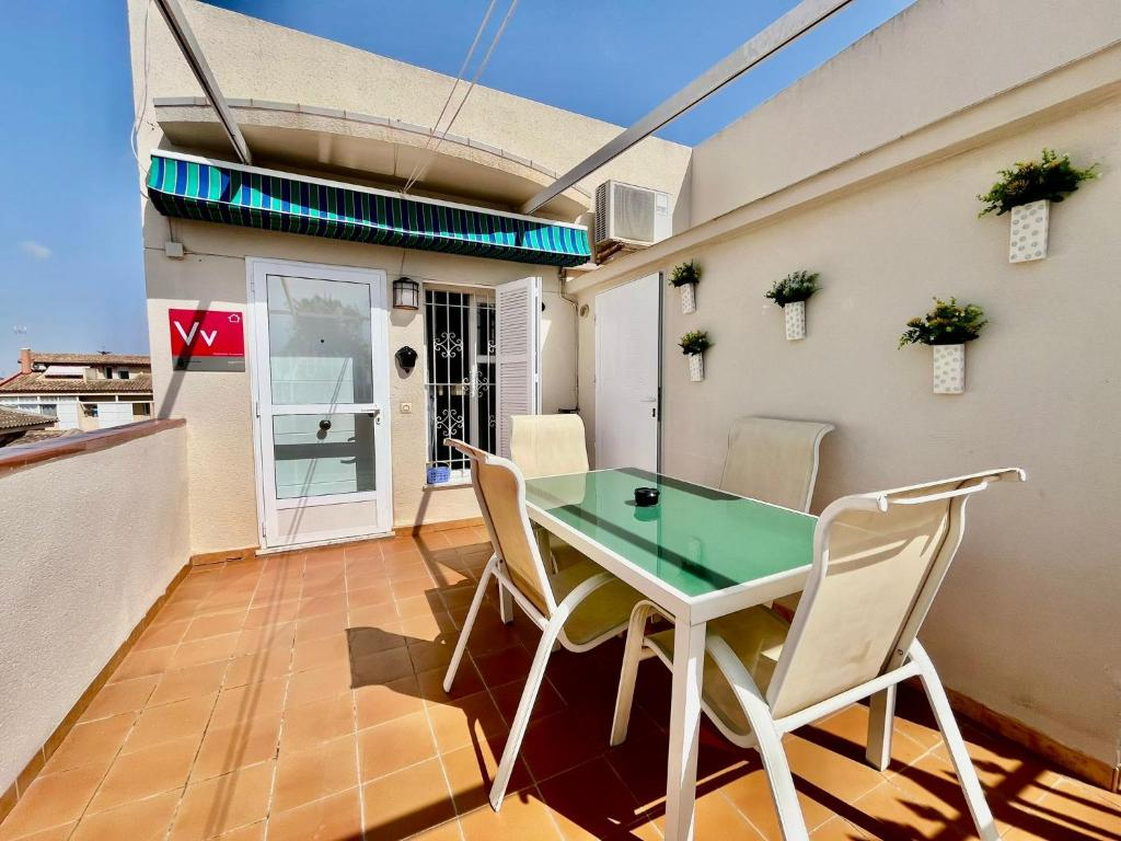 Terraza privada con toldo de rayas, mesa de cristal y cuatro sillas, con la placa Vv junto a la puerta